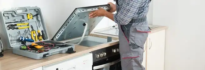 Cooktop repair technician lifting a built-in stovetop for service in Sacramento, CA