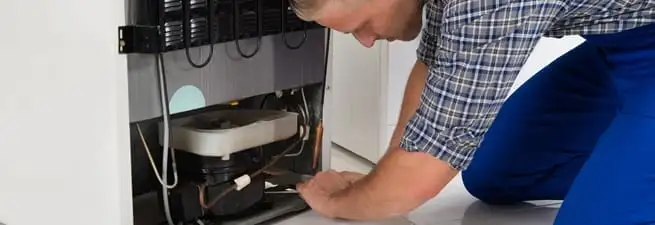 Refrigerator repair technician servicing the compressor and condenser area in Sacramento, CA