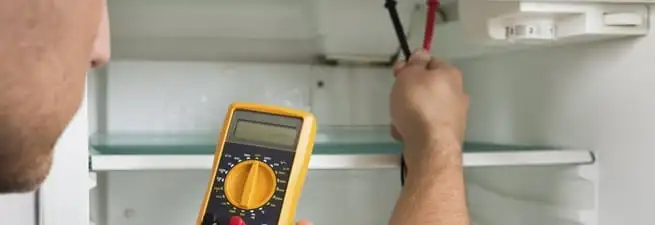 Refrigerator repair technician testing electrical components with a multimeter in Sacramento, CA