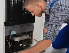 Refrigerator repair technician servicing the compressor and condenser area in Sacramento, CA